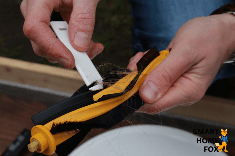 Волосы удаляются с основной щетки робота-пылесоса с помощью чистящего инструмента